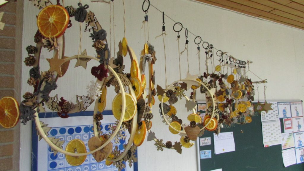 Winterliche Deko aus hängenden Reifen mit Schneeflocken, Sternen, Tannenbäumen und getrocknete Orangenschalen und kleinen Hutzeln.