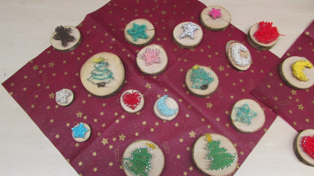 Schnurbbilder auf Baumscheiben. Die Motive sind Sterne, Monde, Herzen, Tannenbäume mit Schmuck.