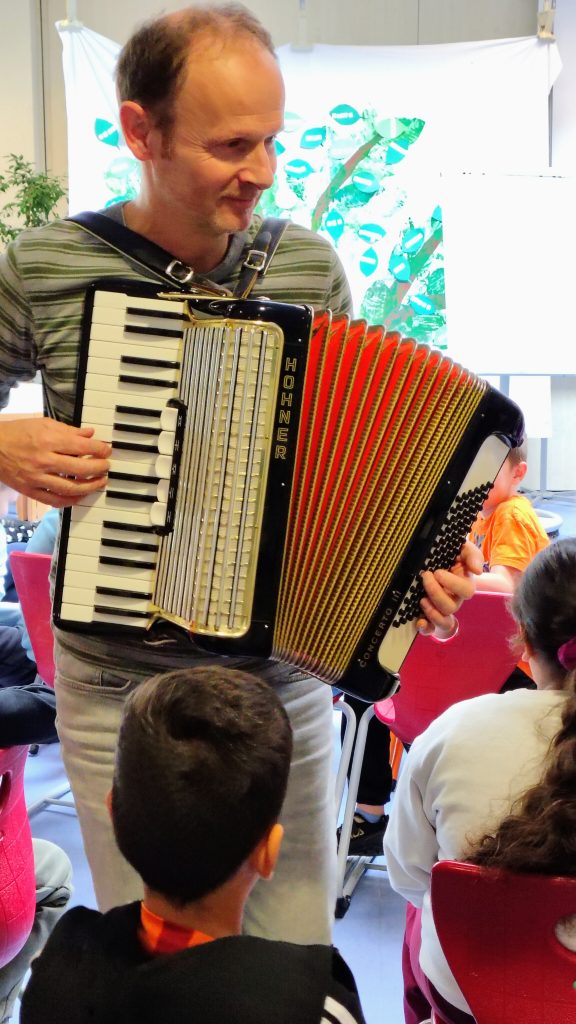 Schüler und Schülerinnen hören einem Akkordeonspieler zu.