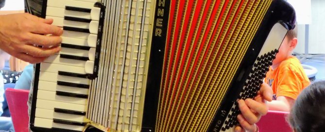 Schüler und Schülerinnen hören einem Akkordeonspieler zu.